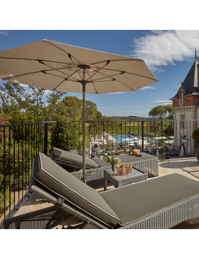 Two rattan sun loungers and a coffee table and parasol  on a southern French terrace overlooking a chateau and a pool