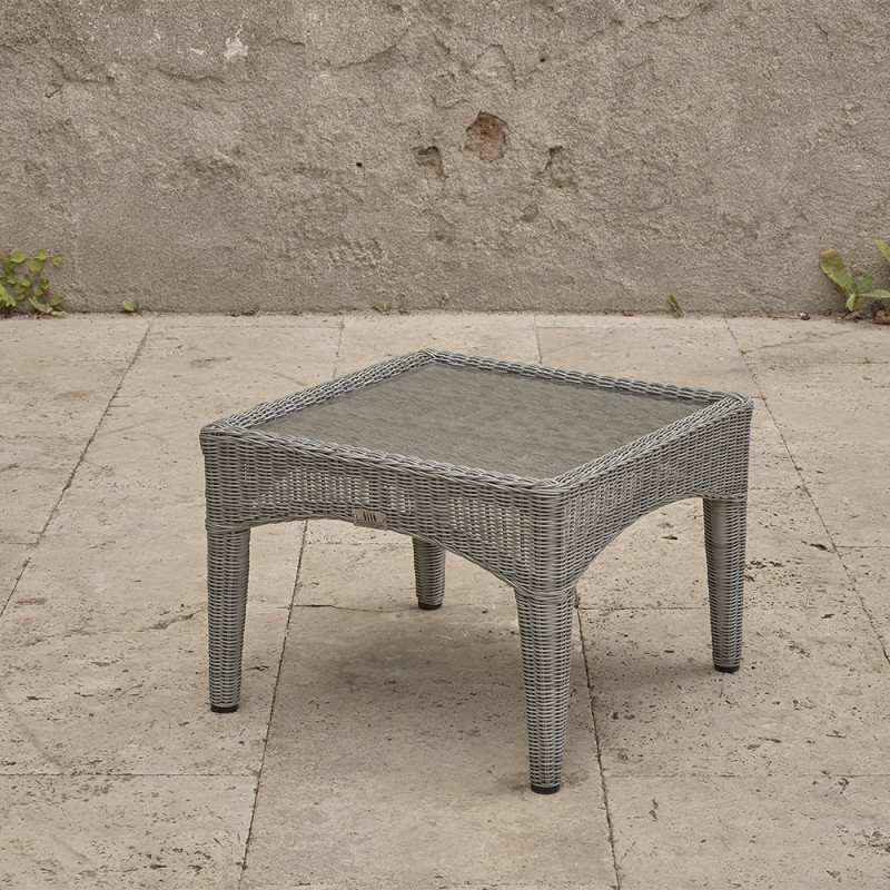 Compact garden rattan side table wirh tempered glass top pictured at an angle on a southern French terrace