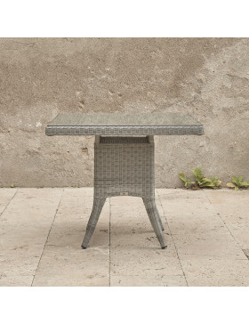 Four seater Grey rattan garden table. On a terrace in front of stone wall