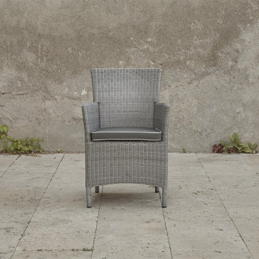 Grey rattan dining chair. On a terrace in front of stone wall